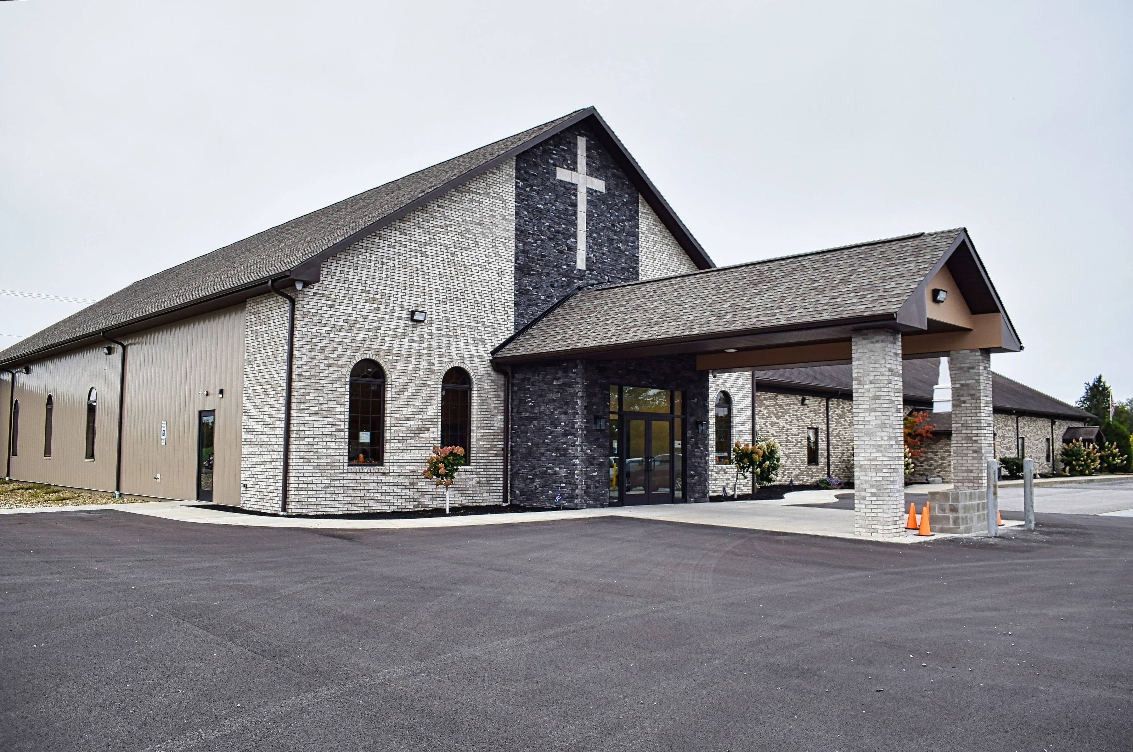 The new sanctuary of Roseville Independent Chapel in Brookville, Pennsylvania — light and charcoal stone, a white cross on the gable, and a covered entrance