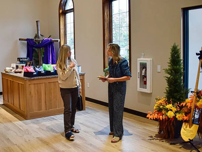 Two women talking in the lobby beside the welcome table and a draped wooden cross