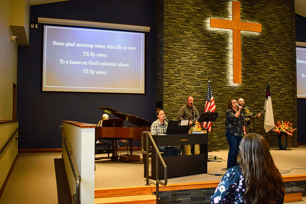 The worship team leading a hymn beside the grand piano, lyrics on the screen above